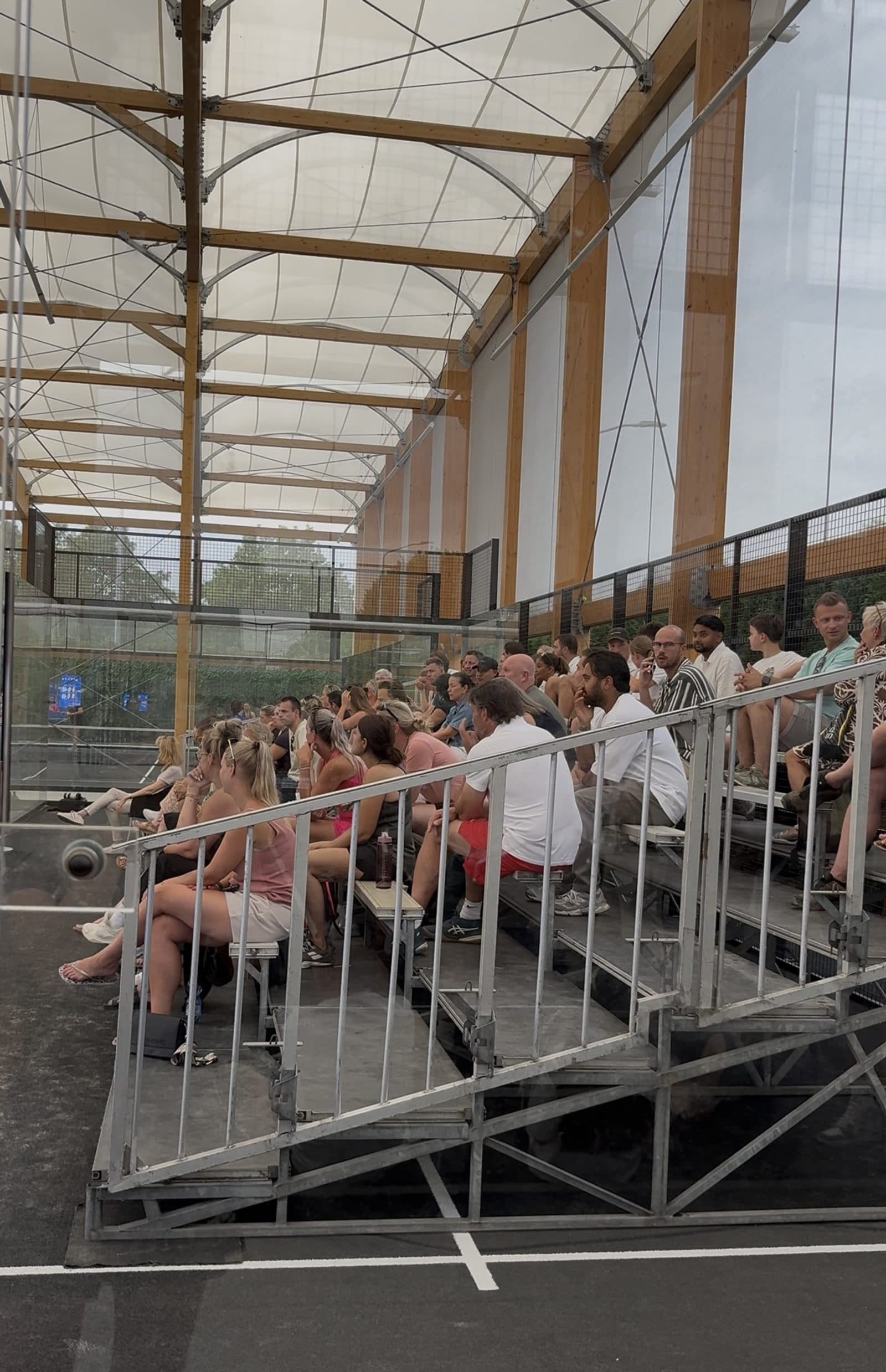Volle tribune langs een overdekte padelbaan tijdens een toernooi