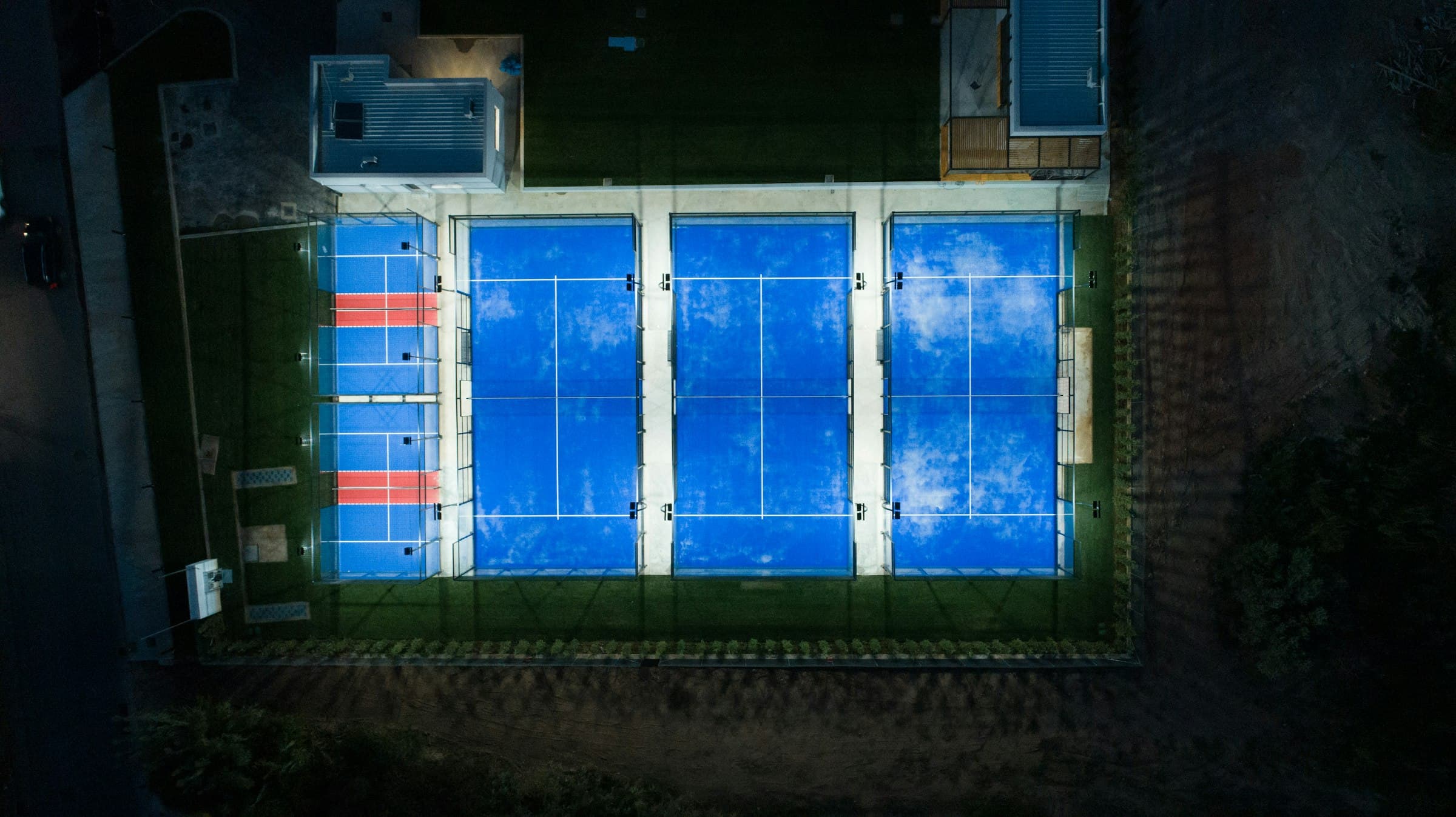 De verlichte padelbanen van TopSpinPlaza van bovenaf in de avond