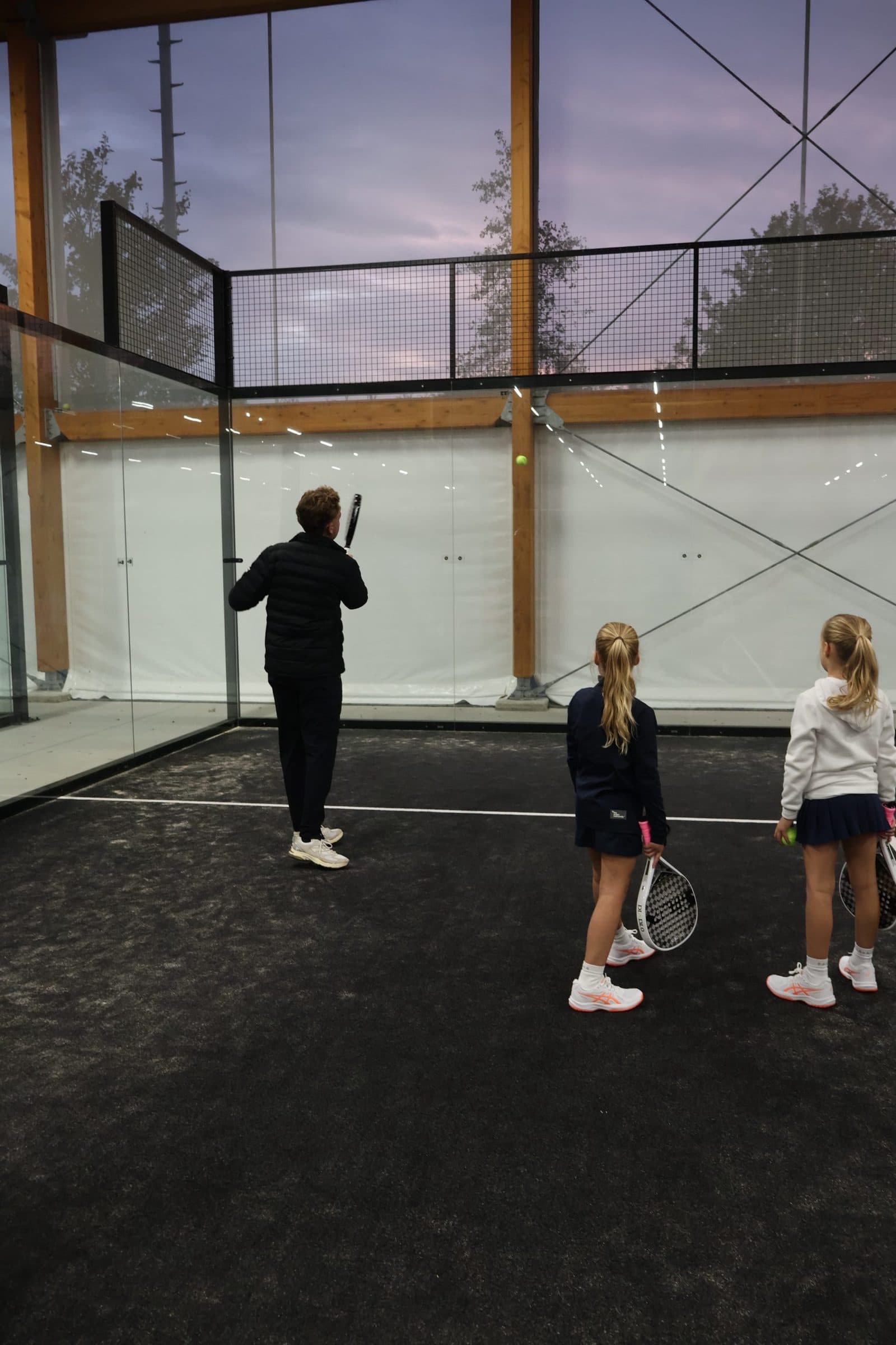 Trainer geeft padelles aan een jonge speler