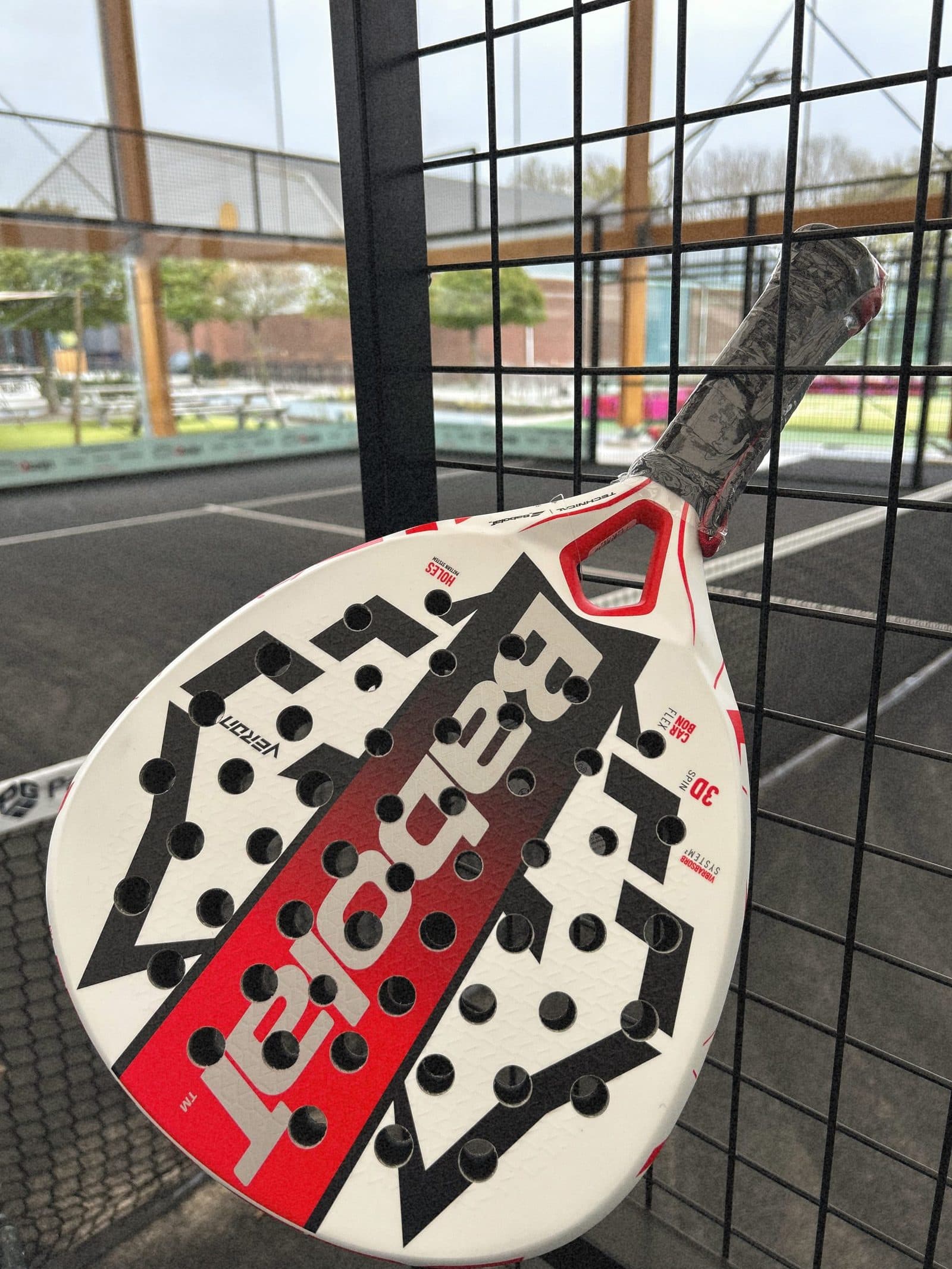 Babolat padelracket aan het hek bij de banen