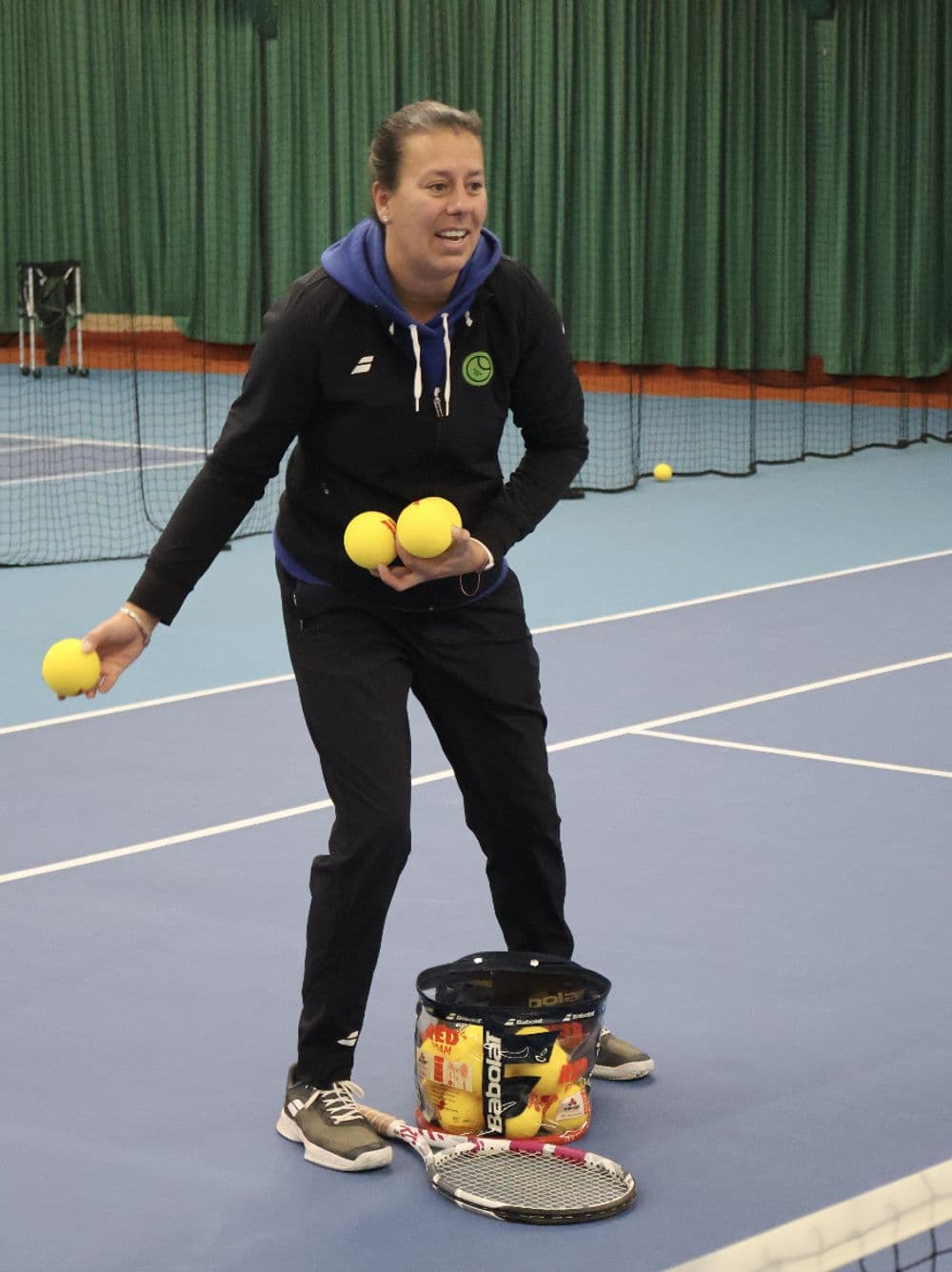 Tennistrainer met ballen tijdens een clinic op een indoorbaan van TopSpinPlaza